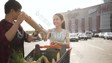 嘲笑美丽的亚洲夫妇，他们手里拿着装满不同用<strong>品</strong>的<strong>购</strong>物车站在大超市附近